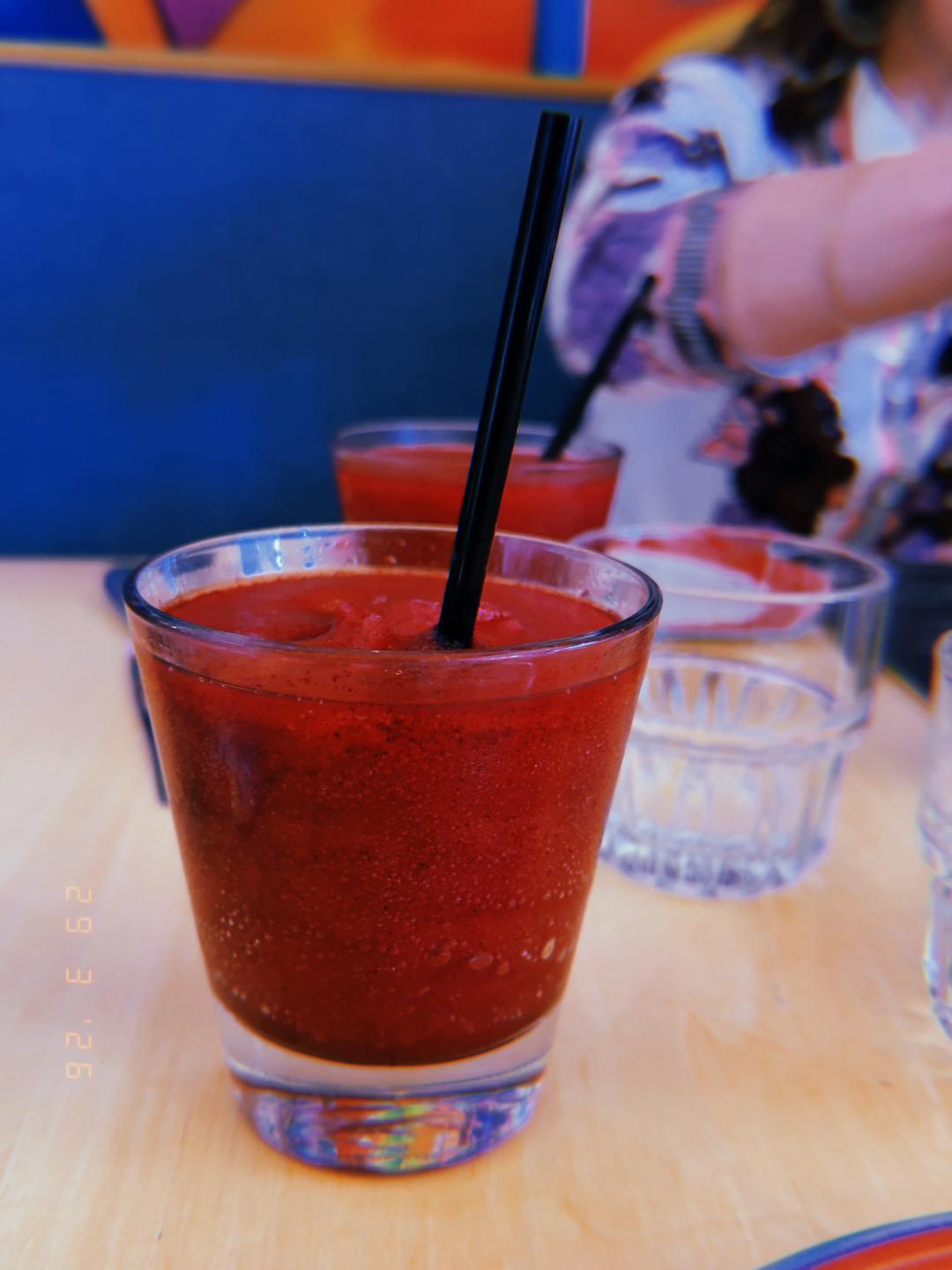 Blueberry frozen margarita in a clear glass with black straw, cobalt blue wall behind